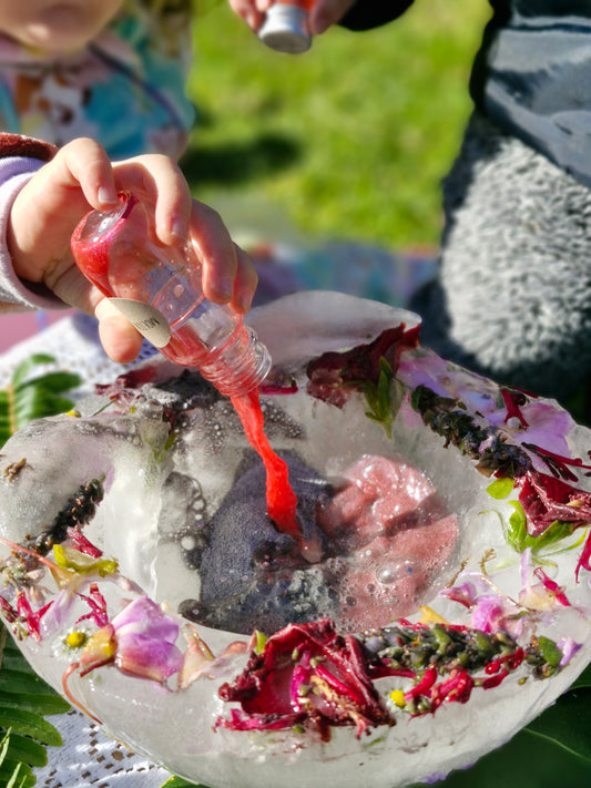 Person holding a small bottle with a red liquid next to a decorative stone with flowers and crystals.