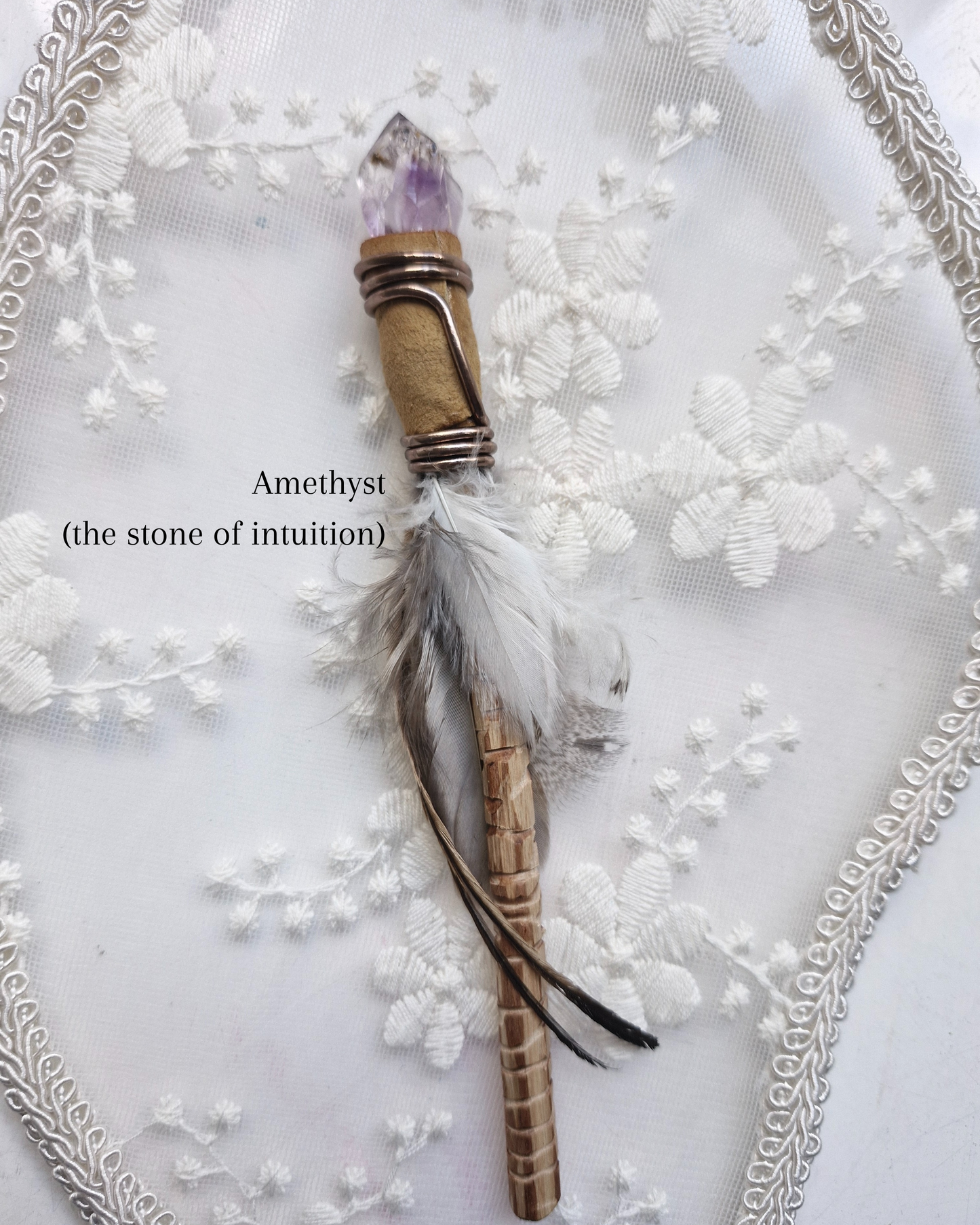 Amethyst crystal wand with feathers on a decorative white background