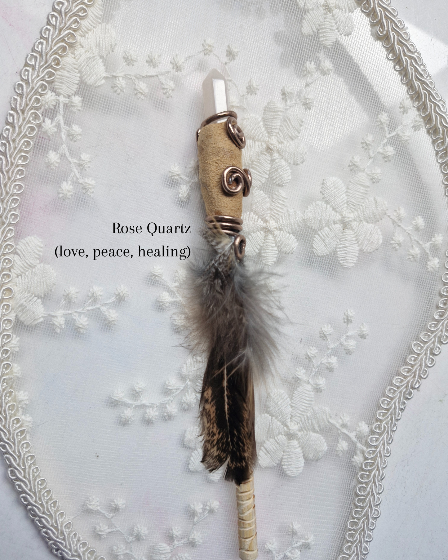 Decorative wand with feathers and rose quartz crystal on a textured white background