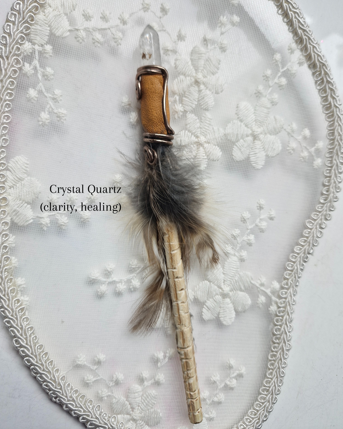 Crystal quartz wand with feather on a decorative white background