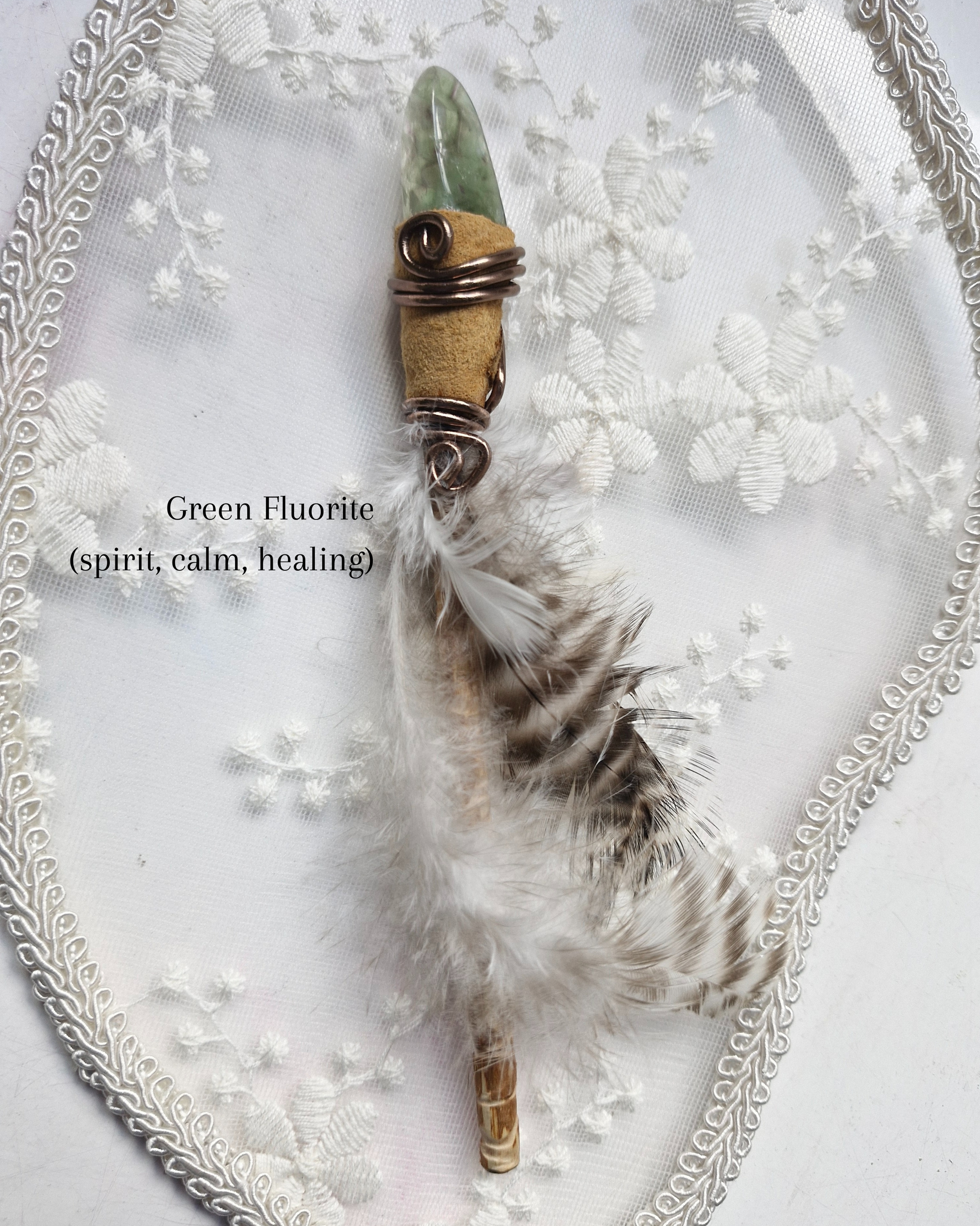 Green Fluorite crystal wand with feathers on a decorative white background