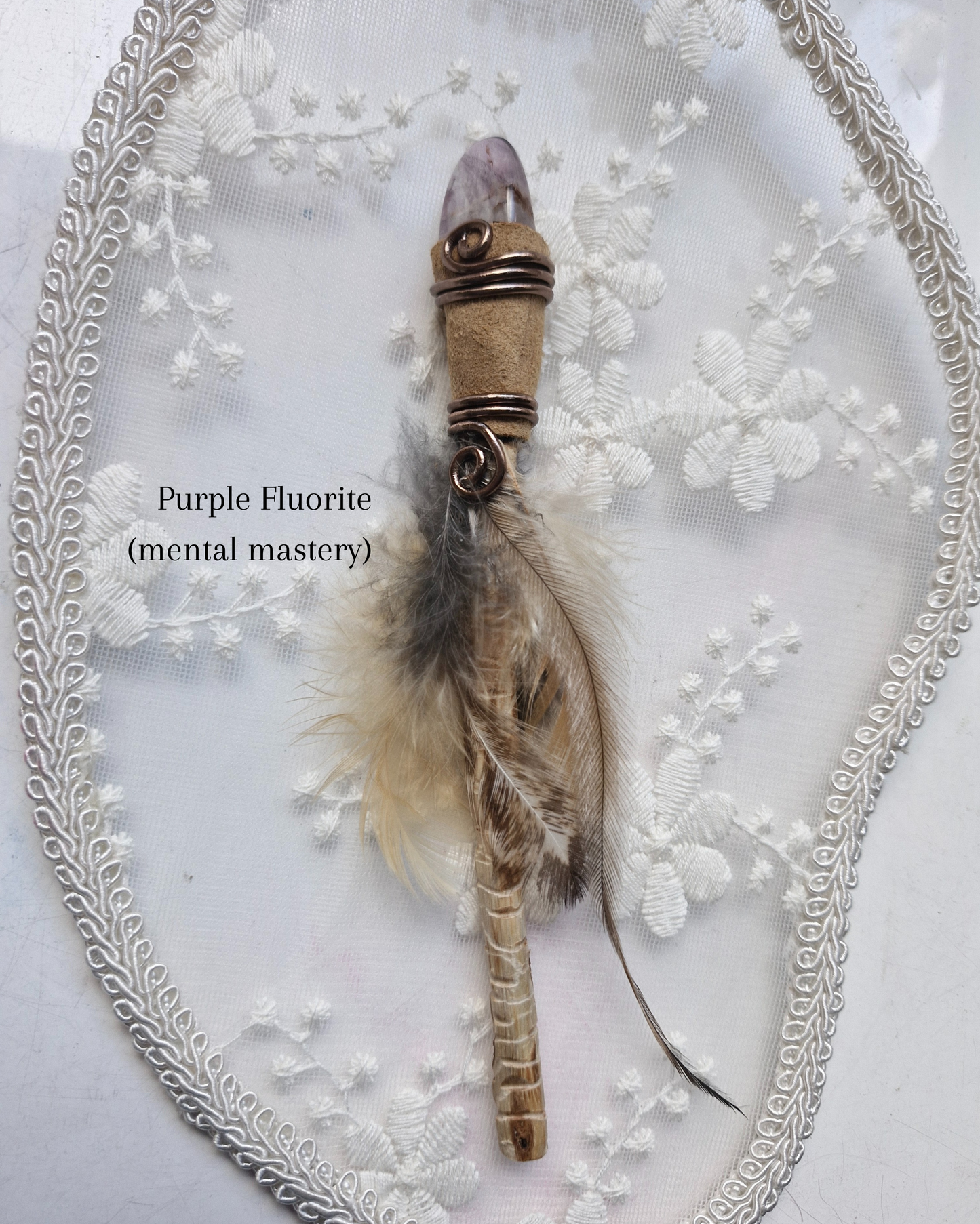 Purple Fluorite crystal wand with feathers on a decorative white background